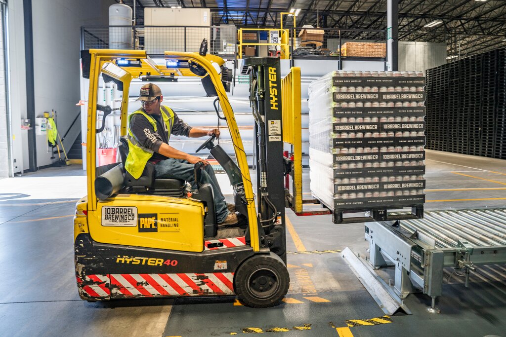 Operator driving a yellow electric Hyster forklift with a pallet inside a warehouse